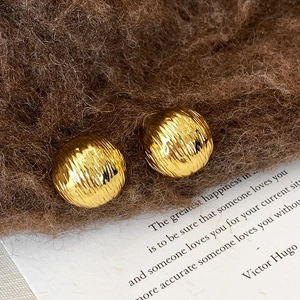 Vue détaillée de boucles d'oreilles boules dorées avec une texture métallique verticale