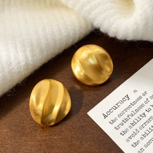 Detail of matte gold irregular round earrings with brushed finish and wavy texture