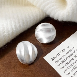 Close-up of silver pleated round earrings with brushed metal texture on soft knit background