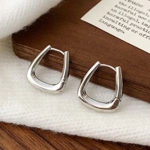 Close-up of polished silver U-shaped geometric hoop earrings on a textured backdrop