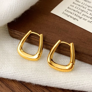 Macro shot of minimalist gold geometric U-shaped hoop earrings on textured white fabric