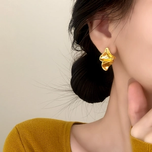 Golden irregular wrinkled stud earrings with liquid metal texture on a female model