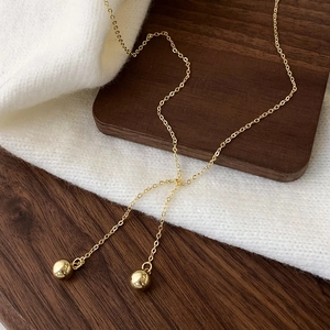 Detail of gold Y-shaped necklace with dual polished spherical pendants on knit fabric