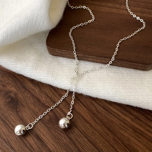 Detail of silver Y-shaped tassel necklace with polished metal beads on knit fabric