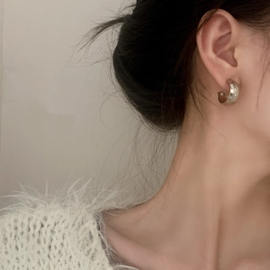 Minimalist textured silver C-shaped hoop earrings on female model with side view