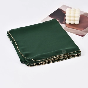 Detail of dark green chiffon hijab featuring elegant gold chain trim on a magazine