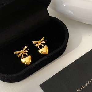 Detail of gold bow earrings with heart pendants on black velvet jewelry display