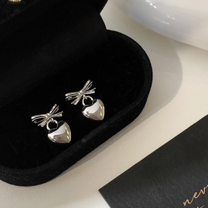 Macro shot of silver bow and heart earrings on black velvet in a luxury gift box