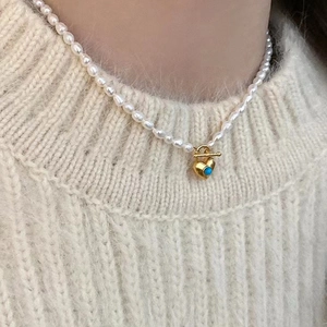 Gros plan d'un collier en perles d'eau douce avec pendentif cœur doré et turquoise sur modèle