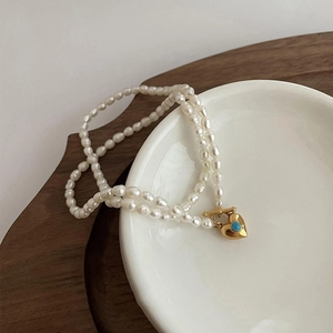Détail du collier de perles avec pendentif cœur et pierre turquoise sur plat blanc