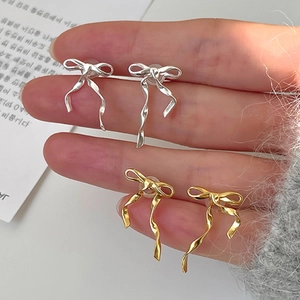 Elegant gold and silver ribbon bow stud earrings set shown against a minimalist background