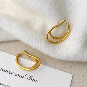 Detailed view of matte gold double-layered ear cuff earrings on white knit fabric