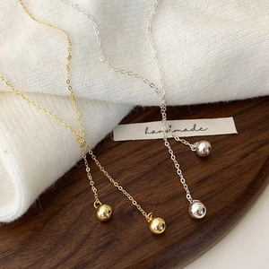 Elegant gold and silver ball pendant necklaces on a minimalist soft white knit background