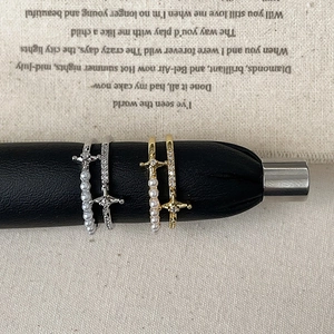 Double-layered pearl cross rings in gold and silver finish on a display stand