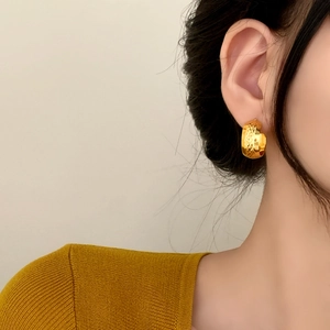 Boucles d'oreilles créoles larges dorées avec motif treillis portées par un mannequin