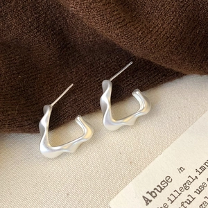 Macro detail of irregular wave-shaped matte silver earrings on soft textured fabric