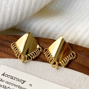 Detail of gold geometric earrings with spiral tassel fringe on a wooden tray
