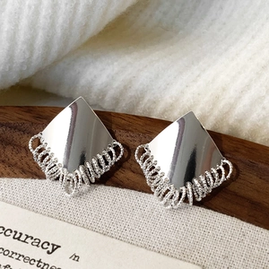 Detailed close-up of geometric diamond earrings with metallic tassels on a wooden tray