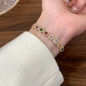 Bracelet luxueux en or avec pierres précieuses carrées colorées porté au poignet sur fond doux