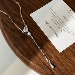 Elegant silver necklace with water drop zircon and pearl pendant on a wooden plate