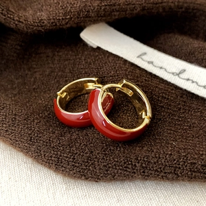 Minimalist gold hoop earrings with red enamel finish on warm knitted background