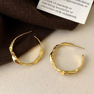 Detail of gold irregular lava-textured hoop earrings on a soft fabric background