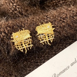 Detail of gold zircon earrings with wrinkled texture and hollow mesh on brown fabric