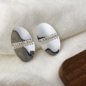 Detail of silver oval stud earrings with textured chain center on a soft knit background