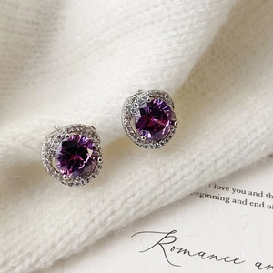 Detail of round purple zircon halo stud earrings set on a white knitted sweater