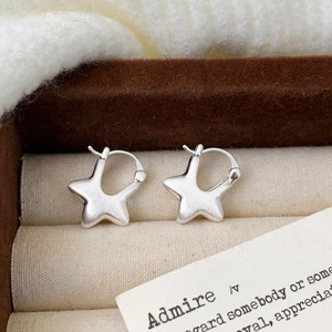 Close-up of matte star-shaped earrings with brushed silver texture on beige fabric