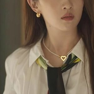 Elegant pearl necklace with a hollow gold heart pendant worn on a model with a silk scarf
