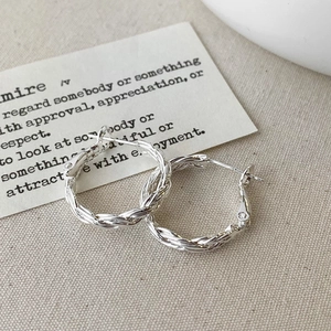Gros plan de créoles en argent torsadées au design spirale sur fond en tissu de lin