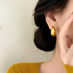 Elegant gold teardrop earrings with a brushed matte finish on a minimalist model