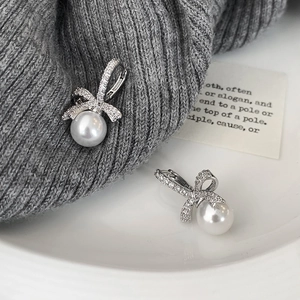 Boucles d'oreilles nœud et perle avec micro-incrustations de zircone sur tricot gris