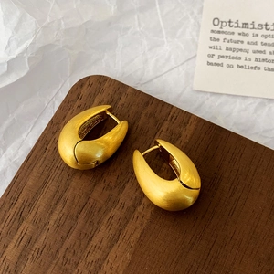 Macro shot of matte gold teardrop hoop earrings with brushed texture on a wood display