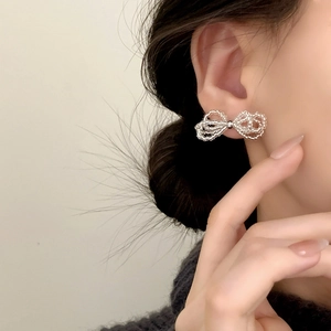 Minimalist silver bow knot stud earrings made of small metal beads on a model's ear
