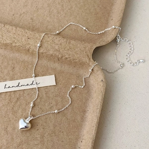 Minimalist silver heart pendant necklace with beaded chain on a rustic textured tray