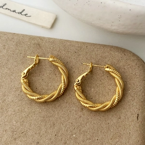 Vue détaillée de boucles d'oreilles créoles torsadées dorées avec un design tressé