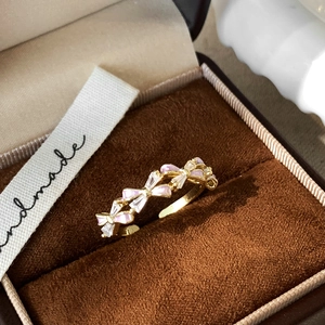 Detail of gold bow ring with pink enamel and zircons on brown velvet jewelry box