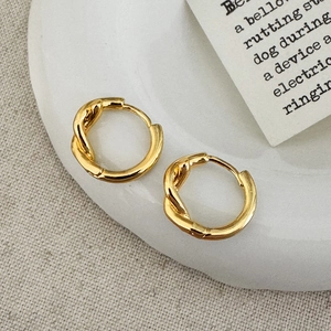 Minimalist twisted hoop earrings in shiny gold finish on elegant white display