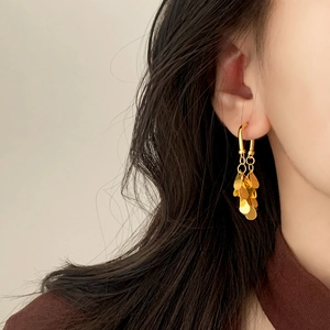 Boucles d'oreilles dorées à pampilles avec feuilles en métal sur crochets en U portées par un mannequin