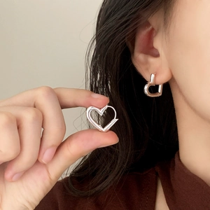 Minimalist silver hollow heart earrings worn on ear to show stylish and elegant scale