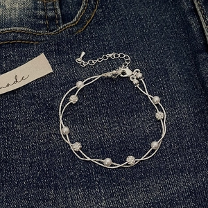 Close-up of double-layer silver bracelet with pearls and crystals on denim background