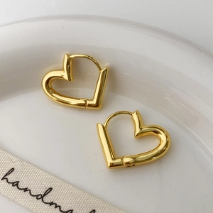 Close-up of minimalist heart-shaped hoop earrings in gold finish on a ceramic plate
