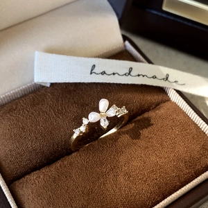 Close-up of pearl and zircon butterfly ring on dark brown velvet with a handmade ribbon