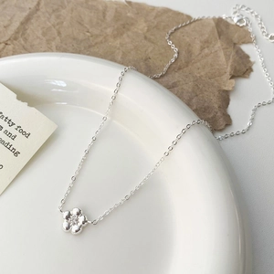Gros plan du collier fleur argenté avec fermoir mousqueton sur une assiette blanche