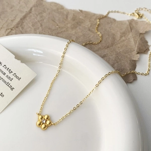 Detailed shot of a delicate gold flower pendant necklace with zircon on a white plate