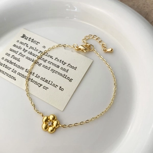 Détail d'un bracelet fleur dorée avec zircon central sur une assiette blanche