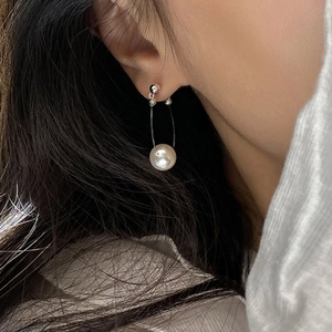 Close-up of elegant pearl drop earring featuring a metallic U-shaped frame on ear