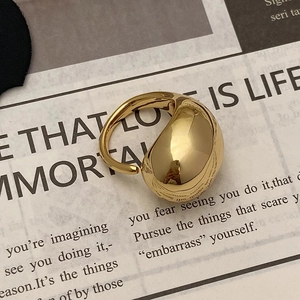 Detailed view of an exaggerated polished gold egg-shaped geometric ring on a newspaper